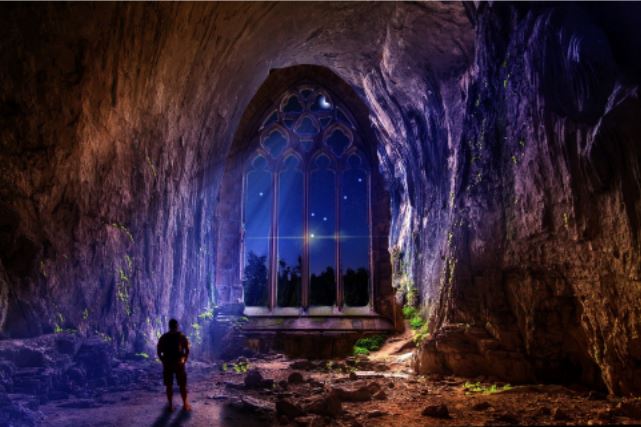 Silhouette of a person standing in a dark cave with an arched catherdral window, light beaming in from the starry sky